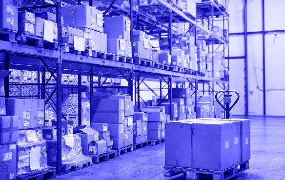 Imagen de un almacén con cajas y paletas de diferentes tamaños, indicando la variedad de mercancías almacenadas.