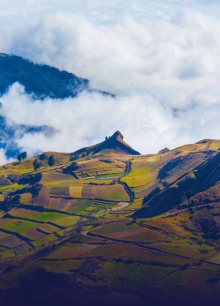 Vista aérea de un paisaje montañoso cubierto de niebla en Ecuador, con campos verdes y colinas onduladas.