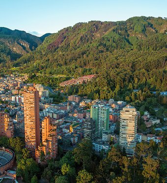 Una ciudad vibrante rodeada de montañas verdes, con edificios de diferentes colores y un cielo azul claro.