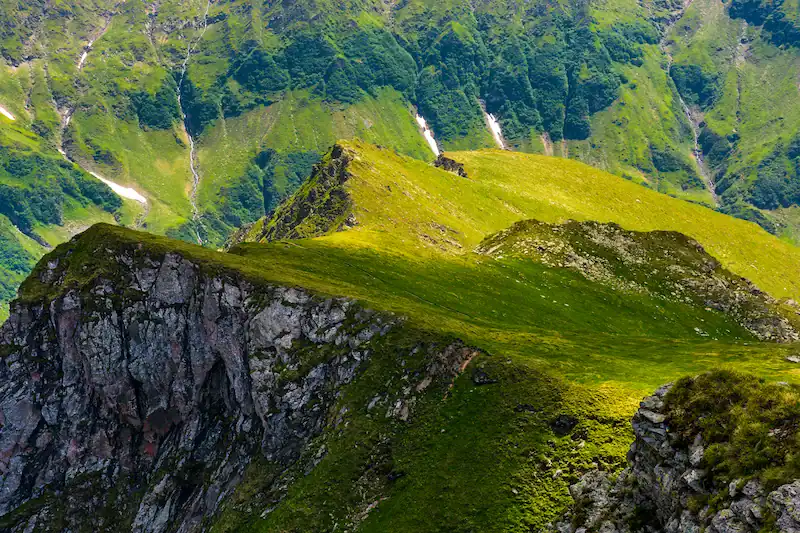 Una vista panorámica de un paisaje montañoso cubierto de vegetación verde, con una formación rocosa en el fondo y nieve en la cima de la montaña.