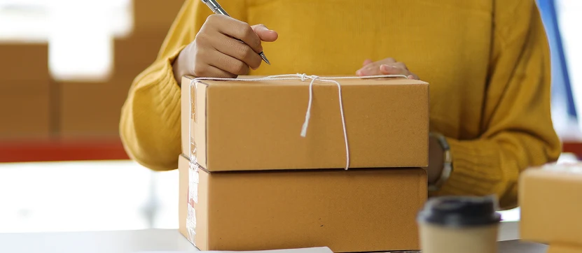 Persona colocando un documento en una caja de cartón en un entorno de envío de paquetería internacional.