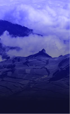 Una vista panorámica de un paisaje montañoso bajo un cielo azul profundo, con árboles verdes diseminados en la zona inferior.