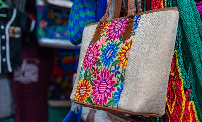 Una bolsa de mano colorida con diseño floral colgada de un gancho en un entorno de mercado.